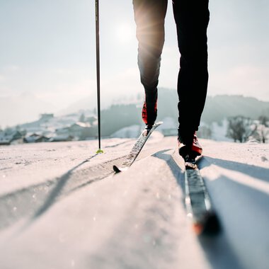 Cross-country skier on the Schwarzwasserloipe trail in Kleinwalsertal, focusing on skis and lower body, on a sunny winter day. | © Kleinwalsertal Tourismus eGen • Photographer: Oliver Farys