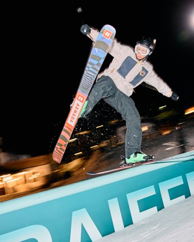 Mann beim Nachtskifahren im Kleinwalsertal, springt mit Skiern über eine Absperrung im Dunkeln, beleuchtet von Scheinwerfern. | © Kleinwalsertal Tourismus eGen • Fotograf: Oliver Farys