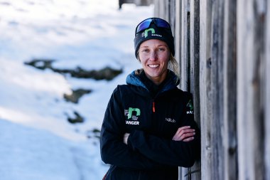 Frau in Winterkleidung mit Sonnenbrille und Mütze steht im Schnee neben einer Holzlounge. | © Kleinwalsertal Tourismus eGen • Fotograf: Oliver Farys