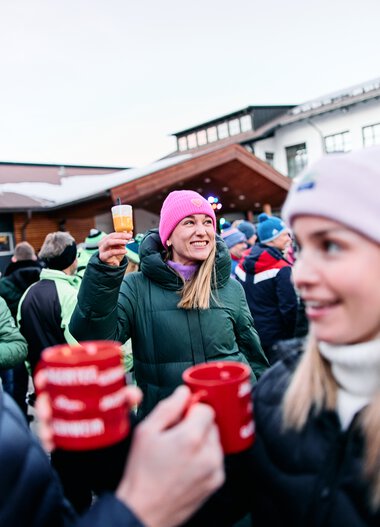 Menschen feiern draußen im Winter, einer hält ein Glas, alle tragen warme Kleidung und Mützen. | © Kleinwalsertal Tourismus eGen • Fotograf: Oliver Farys
