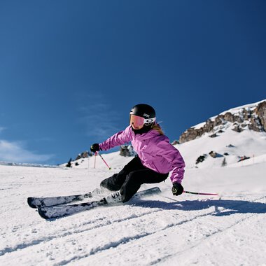 Mädchen beim Skifahren im Schnee in den Alpen, trägt Schutzhelm und pinke Jacke bei schönem Winterwetter. | © Kleinwalsertal Tourismus eGen • Fotograf: Oliver Farys