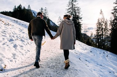 Ein Paar wandert im Schnee auf einer Winterwanderung im Kleinwalsertal, hält Händchen und genießt die verschneite Landschaft. | © Kleinwalsertal Tourismus eGen • Fotograf: Oliver Farys