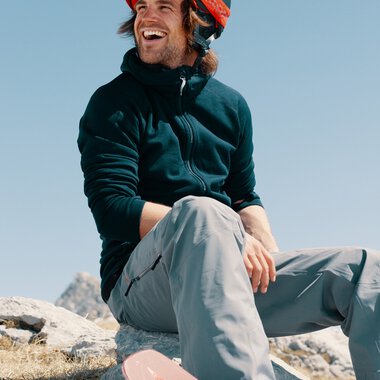 Junge Mann mit Helm und Skihandschuhen, lachend im Schnee, sitzt vor einem Skilift | © Kleinwalsertal Tourismus eGen • Fotograf: Distillery
