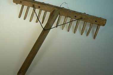 Ein hölzernes Rechen mit langen Nägeln, vermutlich aus historischer Landwirtschaft. Es hat einen Griff und ist an einem Seil befestigt. | © Kleinwalsertal Tourismus eGen • Stefan Heim