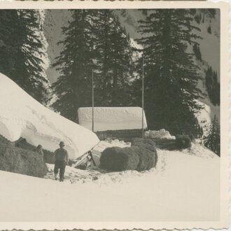 Historische Schwarz-Weiß-Aufnahme eines Hauses in verschneiter Landschaft, umgeben von Tannenbäumen, mit einem Menschen davor. | © Kleinwalsertal Tourismus eGen • Stefan Heim