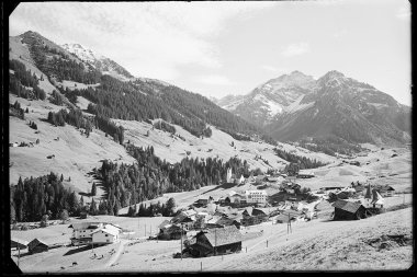 Historisches Schwarz-Weiß-Foto des Dorfes Hirschegg im Kleinwalsertal mit Kirche, umgeben von Bergen und Wiesen in den Alpen. | © Kleinwalsertal Tourismus eGen • Karl Max Kessler Archiv