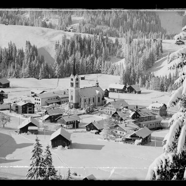 Historisches Foto des verschneiten Riezlern mit Kirche im Zentrum, umgeben von Bergen. | © Kleinwalsertal Tourismus eGen • Karl Max Kessler Archiv