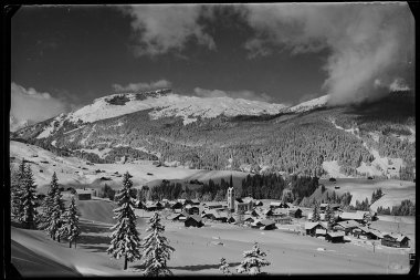 Schöne schwarze und weiße Fotografie von Riezlern auf 1100 m Höhe, umgeben von verschneiten Bergen und Tannen im Winter. | © Kleinwalsertal Tourismus eGen • Karl Max Kessler Archiv
