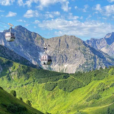 Sommerliche Kanzelwandbahn mit Gondeln im Alpenpanorama, grüne Hügel, Berge und blauer Himmel. | © Oberstdorf · Kleinwalsertal Bergbahnen