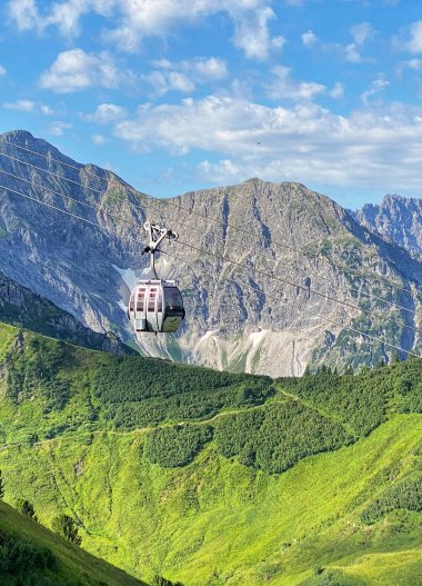 Summer Kanzelwand cable car with gondolas in the alpine landscape, green hills, mountains, and blue sky. | © Oberstdorf · Kleinwalsertal Bergbahnen