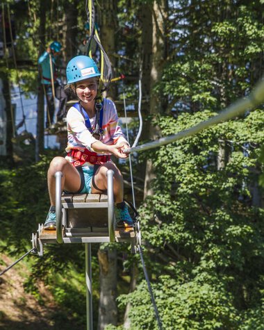 Young woman at Söllereck climbing garden on a zip line, wearing a helmet and smiling. | © Oberstdorf · Kleinwalsertal Bergbahnen