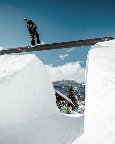 Skateboarder jumping over a snow gap with snow walls on both sides, under clear sky. The scene is set on a winter ski slope. | © Kleinwalsertal Tourismus eGen • Crystal Ground • Photographer: Stefan Eigner