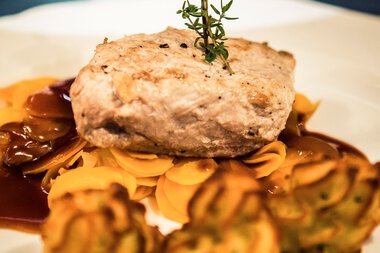 Stuffed meatball on a plate with flowers and vegetables, garnished with a sprig and a flower. | © Kleinwalsertal Tourismus eGen • Photographer: Oliver Farys