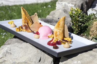 Ein elegantes Dessert auf einem langen weißen Teller mit Eis, Fruchtpüree, Creme, Baiser und Dekoration, im Freien auf einem Steintisch.  | © Kleinwalsertal Tourismus eGen • Fotograf: Frank Drechsel