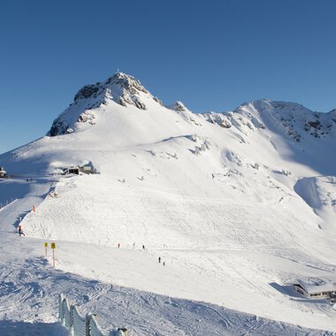 Verschneite Berge in einem Skigebiet mit blauer Himmel, Pisten und Skiliften. | © Kleinwalsertal Tourismus eGen