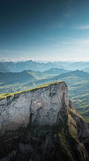 Berglandschaft mit grünen Hügeln und steilen Klippen unter einem blauen Himmel, aufgenommen vom Ifen. | © Kleinwalsertal Tourismus eGen • Fotograf: Robert Niederwolfsgruber