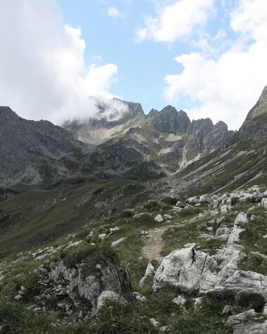 Berglandschaft mit Gipfeln, Steinen und Grünflächen unter einem partly bewölkten Himmel. | © Kleinwalsertal Tourismus eGen • Fotograf: Antje Pabst