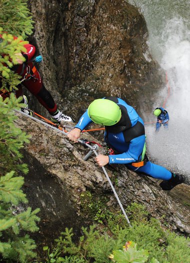 Menschen beim Canyoning in einer engen, steilen Felswand, Wasser stürzt herab, alle tragen Helme und Schutzkleidung. | © Rocksolid
