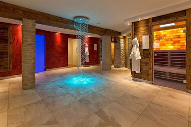Innenraum eines Spa- oder Wellnessbereichs mit Wasserfall, ansprechender Beleuchtung und Saunapositionen. | © Aparthotel
