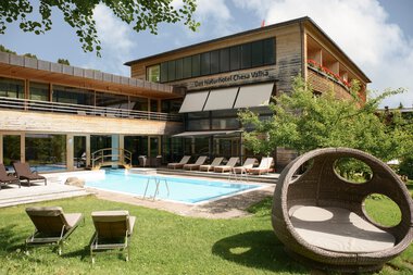 Das Naturhotel Chesa Valisa mit Außenpool, Liegestühlen und Garten im Sonnenlicht, umgeben von Bäumen. | © Naturhotel Chesa Valisa