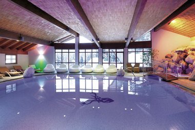 Innenaufnahme eines Wellnessbereichs mit einem Pool, Liegen und Fenster, die viel Tageslicht hineinlassen. | © Walserhof