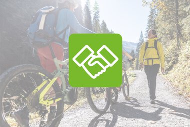 Zwei Fahrradfahrer und ein Wanderer auf einem Waldweg, bei Sonnenschein, umgeben von Bäumen. | © Kleinwalsertal Tourismus eGen