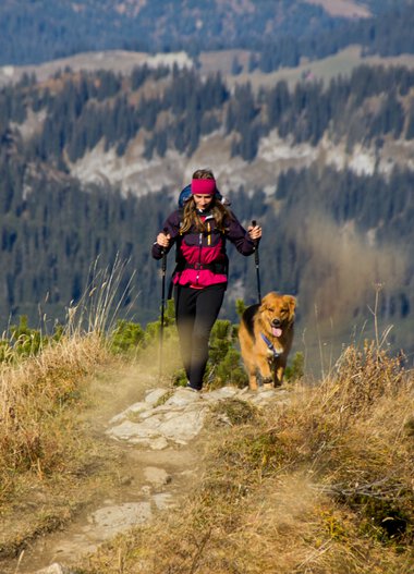 Frau wandert mit Hund auf einem Wanderweg in den Bergen im Herbst. | © Kleinwalsertal Tourismus eGen • Fotograf: Lukas Rinner