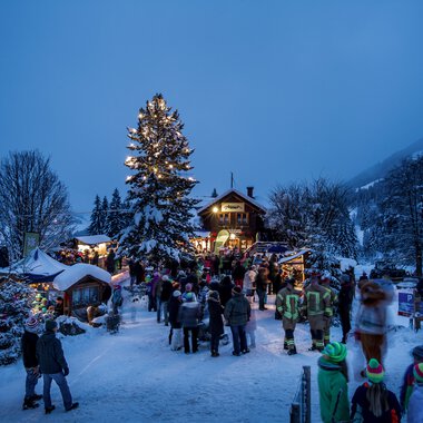 Festive winter event at the Advent magic with visitors, Christmas trees, and festive lights in a snowy landscape. | © Kleinwalsertal Tourismus eGen • Photographer: Dominik Berchtold